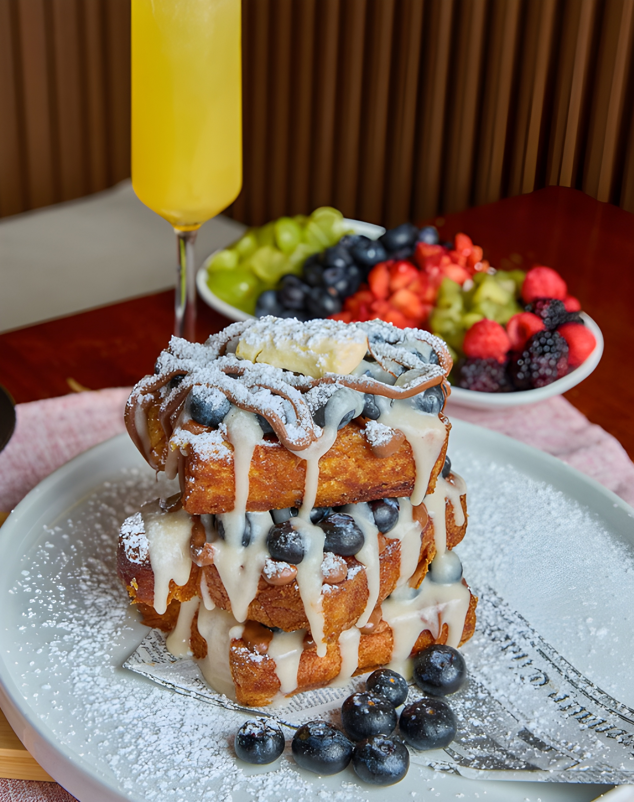 A tall stack of French toast with blueberries, cream and powdered sugar